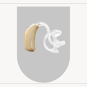 Puede incluir: Un audífono beige y transparente. El dispositivo tiene un diseño curvo con un molde de oído transparente y la marca "PHONAK" impresa en el lateral. El audífono está diseñado para colocarse detrás de la oreja.