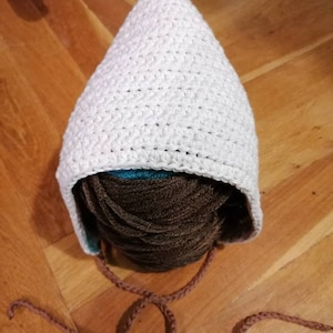 Könnte beinhalten: Weißer Häkelhut mit braunen Garnbändern. Der Hut liegt auf einer Holzoberfläche.