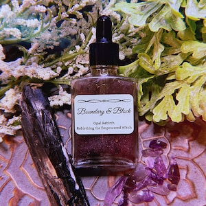 May include: A glass bottle with a dropper filled with a purple liquid. The bottle has a label that reads "Boundary & Block" and "Opal Rebirth Rebirthing the Empowered Witch". The bottle is surrounded by purple crystals and a black stone.