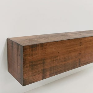 May include: A dark brown wooden mantel shelf with a distressed finish. The shelf is rectangular and has a smooth surface.