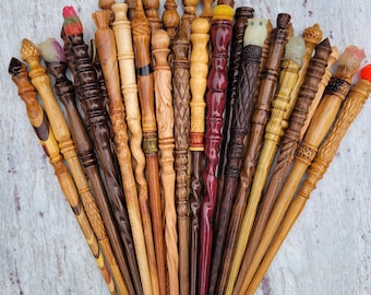 May include: A collection of handcrafted wooden wands arranged in a fan shape. Each wand features unique turned details, varying wood tones from light to dark, and decorative finials including carved shapes and colorful resin accents at the tips.