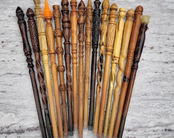 May include: A collection of fifteen handcrafted wooden wands arranged in a fan shape. Each wand features unique carved textures, varying shades of brown and tan wood, and distinct finial designs, including one with a bright orange tip.