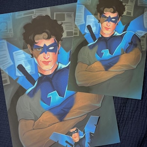Könnte beinhalten: Kunstwerk im Comic-Stil mit einer männlichen Figur in einem blau-schwarzen Superhelden-Kostüm. Das Bild enthält zwei vollständige Drucke und einen kleineren Ausschnitt, die alle dieselbe Figur mit Maske und stilisierten Flügeln zeigen.