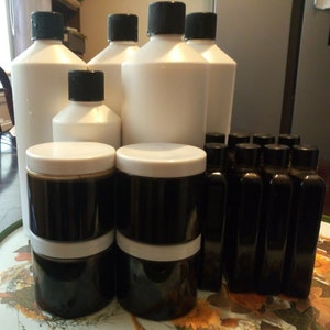 Może przedstawiać: Zbi&oacute;r białych plastikowych butelek i ciemnobrązowych szklanych słoik&oacute;w z białymi pokrywkami. Butelki i słoiki są ułożone w kształcie piramidy na stole z kwiatowym wzorem.