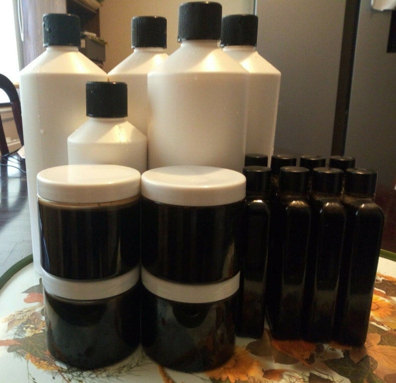 Może przedstawiać: Zbi&oacute;r białych plastikowych butelek i ciemnobrązowych szklanych słoik&oacute;w z białymi pokrywkami. Butelki i słoiki są ułożone w kształcie piramidy na stole z kwiatowym wzorem.