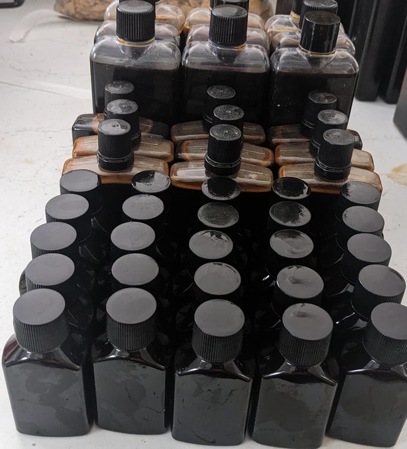 Może przedstawiać: Kolekcja małych, ciemnobrązowych butelek szklanych z czarnymi zakrętkami. Butelki są ułożone w rzędach i kolumnach na białym tle.