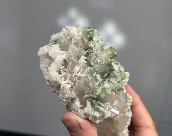 May include: A cluster of green and white crystals on a matrix. The crystals are translucent and have a glassy luster. The matrix is rough and has a brown color.
