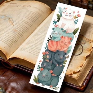 以下が含まれることがあります： さまざまな色の、白、ティール、オレンジ、グレー、緑の笑顔の漫画のハムスターのスタックが特徴の気まぐれなブックマーク。 ブックマークは花と葉で飾られ、開いた本の背景に設定されています。