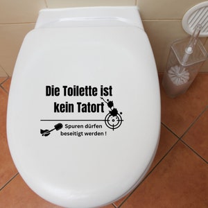 K&ouml;nnte beinhalten: Eine wei&szlig;e Toilettensch&uuml;ssel mit einem schwarz-wei&szlig;en Aufkleber, auf dem "Die Toilette ist kein Tatort" und "Spuren d&uuml;rfen beseitigt werden!" steht, sowie ein Zielsymbol und eine Toilettenb&uuml;rste.
