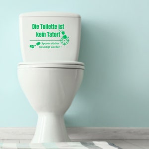 K&ouml;nnte beinhalten: Eine wei&szlig;e Toilette mit einem gr&uuml;nen Aufkleber auf dem Tank, auf dem "Die Toilette ist kein Tatort" und "Spuren d&uuml;rfen beseitigt werden!" steht. Der Aufkleber zeigt eine Zielscheibe und eine Toilettenb&uuml;rste.