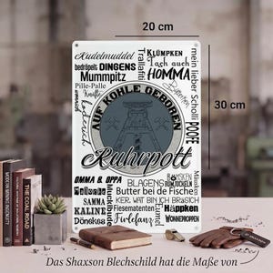 Könnte beinhalten: Ein rechteckiges weißes Metallschild mit den Maßen 20 cm mal 30 cm, das einen grauen Kreis mit einem Förderturm-Motiv und dem Text AUF KOHLE GEBOREN zeigt. Das Schild ist mit zahlreichen deutschen Wörtern und Phrasen in schwarzer Schrift bedruckt.