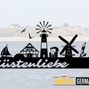 May include: Black silhouette of a lighthouse, windmill, sailboat, house, and a seal on a black background with the text "Küstenliebe MADE IN GERMANY".