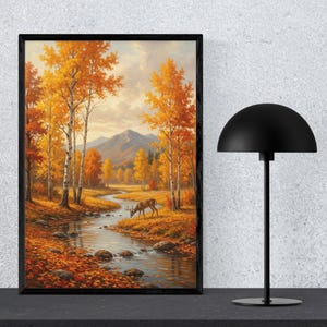 Könnte beinhalten: Gerahmtes Landschaftsbild mit einer Herbstszene mit Fluss, Bäumen und einem Hirsch. Das Kunstwerk zeigt leuchtende Farben von Orange, Gelb und Braun, mit einer Bergkette im Hintergrund. Der Rahmen ist schwarz, und eine schwarze Lampe steht daneben.