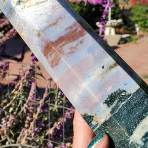 May include: A polished stone tower featuring a multi-colored surface with bands of white, soft pink, and deep rust-orange, transitioning into a dark, textured forest green base with intricate mineral inclusions and a smooth, reflective finish.
