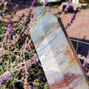 May include: A polished crystal tower featuring a multifaceted point. The stone displays a blend of translucent light blue, milky white, and opaque earthy brown and orange bands with subtle dark mineral inclusions throughout the crystalline structure.