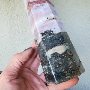 May include: A multi-faceted stone tower featuring a distinct color gradient. The base is a deep, dark forest green with textured mineral inclusions, transitioning upward into layers of soft lavender, pale pink, and white with subtle brown speckling.