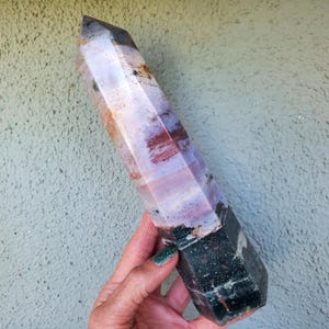May include: A polished, hexagonal crystal tower featuring a color gradient that transitions from a dark, speckled forest green base to a translucent, pale lavender and white midsection, ending in a sharp, semi-transparent, smoky gray point.