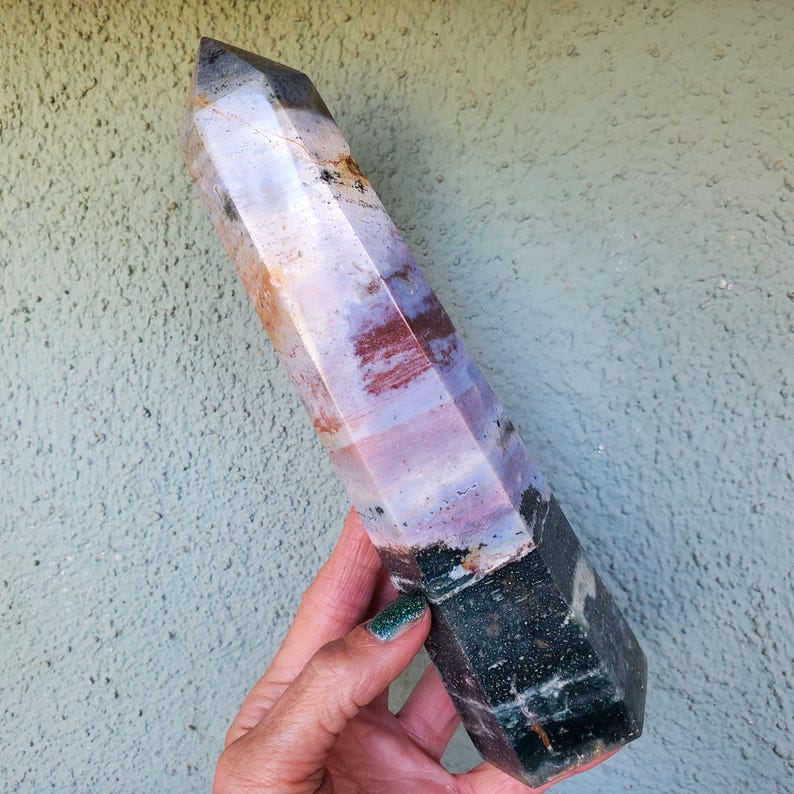 May include: A polished, hexagonal crystal tower featuring a color gradient that transitions from a dark, speckled forest green base to a translucent, pale lavender and white midsection, ending in a sharp, semi-transparent, smoky gray point.