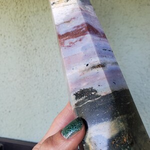 May include: A tall, faceted stone tower featuring a polished surface with horizontal bands of color including white, light purple, deep red, and a solid dark charcoal gray base. The stone displays natural mineral inclusions and varied textures.
