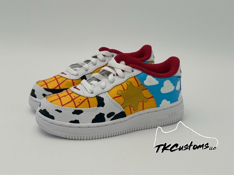 Op de afbeelding: Witte lage sneakers met een aangepast ontwerp met een geel en rood geruit patroon, een zwart-witte koe-print, een gele ster en een blauwe lucht met witte wolken. De sneakers hebben een rode tong en een witte zool.