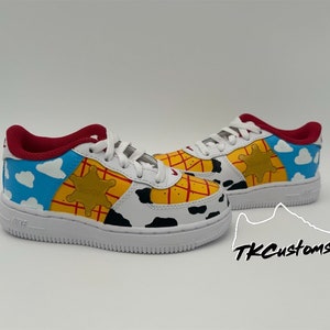 Op de afbeelding: Op maat gemaakte witte sneakers met een ontwerp ge&iuml;nspireerd door het personage Woody uit de Toy Story-franchise. De schoenen hebben een geel, rood en blauw kleurenschema met een sheriffster en wolken.