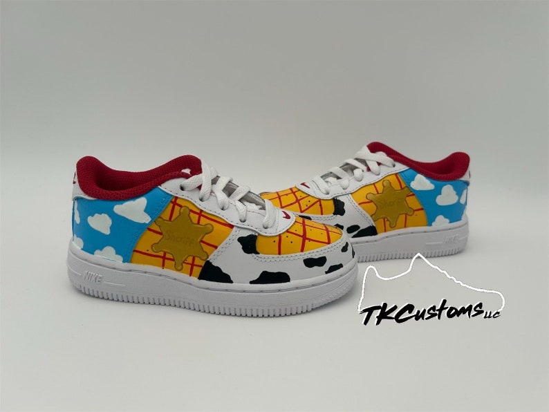 Op de afbeelding: Op maat gemaakte witte sneakers met een ontwerp ge&iuml;nspireerd door het personage Woody uit de Toy Story-franchise. De schoenen hebben een geel, rood en blauw kleurenschema met een sheriffster en wolken.