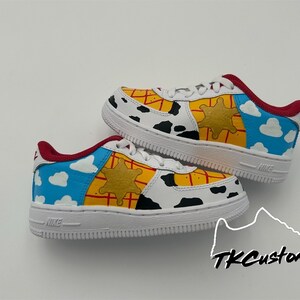 Op de afbeelding: Witte sneakers met een aangepast ontwerp met een Toy Story-thema. De schoenen hebben een blauwe lucht met witte wolken, een gele sheriffster en een rood-geel ruitpatroon.