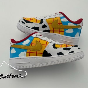 Op de afbeelding: Witte, gele, rode en blauwe custom-gekleurde sneakers met een koe-print ontwerp. De sneakers hebben een rood swoosh-logo en een blauw ontwerp met witte wolken aan de zijkant.