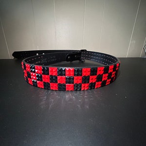 Puede incluir: Un cinturón de cuero negro con un patrón de tablero de ajedrez de tachuelas piramidales rojas y negras.