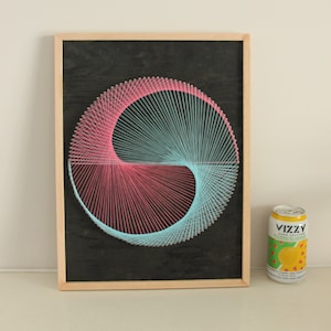May include: A framed string art piece with a pink and blue spiral design on a black background.