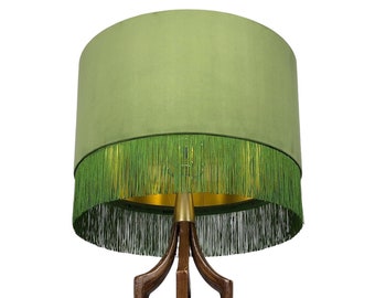 May include: A mid-century modern table lamp with a green velvet lampshade with a fringe trim and a wooden base.