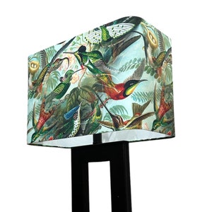 Puede incluir: Una lámpara de pie negra con una pantalla rectangular con un estampado de colibríes coloridos sobre un fondo azul claro.