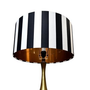 May include: A gold table lamp with a black and white striped lampshade. The lampshade has a gold lining.