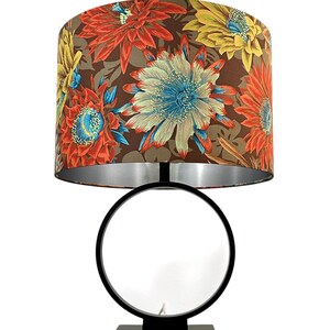 May include: A decorative table lamp with a floral patterned lampshade. The shade features large flowers in shades of red, yellow, and blue against a brown background. The lamp has a black metal base with a circular design and a square base.