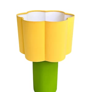 May include: A table lamp featuring a bright yellow, flower-shaped fabric lampshade with a white interior lining, supported by a solid, cylindrical, lime green base. The lamp has a distinct, bold color palette and a smooth, matte finish throughout.