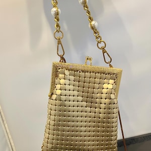 May include: A gold mesh chain bag with a pearl and chain strap. The bag has a rectangular shape and a clasp closure.