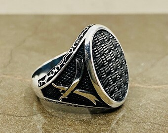 May include: A silver ring with a textured oval design. The ring has a detailed pattern around the band.