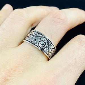 May include: A silver ring with a wide band featuring an intricate floral design.
