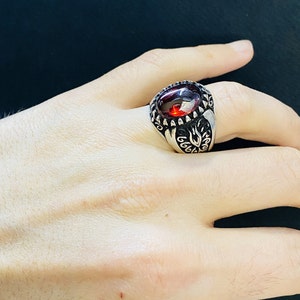 Könnte beinhalten: Ein silberner Ring mit einem verzierten Design und einem großen, roten Edelstein.