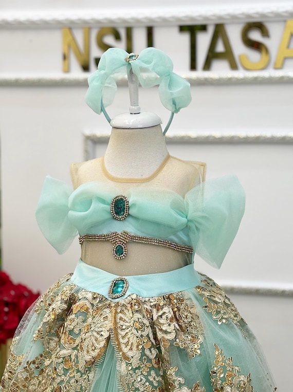gold and mint green dress A mint gown with a high neckline and a daring thigh-high slit, featuring  intricate sequin embellishments in teal and gold that highlight the bodice  and sleeves. The draped silhouette exudes elegance and