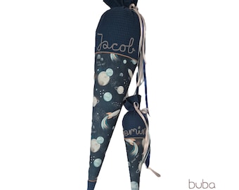 May include: Two navy blue, cone-shaped school bags with a space-themed design. The larger bag has the name "Jacob" embroidered on it, while the smaller bag says "amin". Both bags feature planets, rockets, and stars.