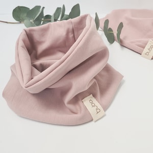 Könnte beinhalten: Ein staubiger rosafarbener Halsschmeichler mit einem braunen Etikett, auf dem "buba" steht.