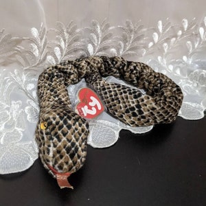 May include: A brown and black snake Beanie Baby with a yellow eye and a red tongue. The snake is curled up and has a red Ty tag attached to it.