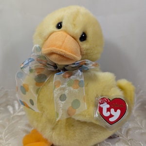 May include: A yellow plush duck with a blue and orange polka dot ribbon around its neck. The duck has a Ty heart tag attached to its wing that says "Beanie Babies".