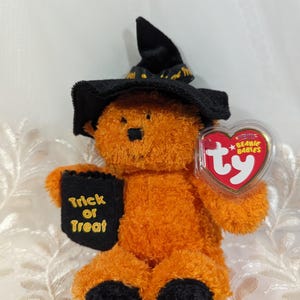 May include: Orange and black Halloween beanie baby wearing a witch's hat, holding a black book that says "Trick or Treat" and a Ty Beanie Babies tag.