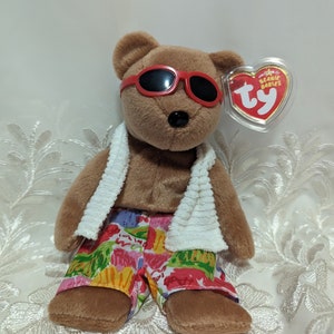 Può includere: Un orsacchiotto di peluche marrone della marca Beanie Baby che indossa occhiali da sole rossi, un asciugamano bianco e pantaloncini da bagno con stampa floreale colorata. L'orso ha un'etichetta Ty Beanie Babies attaccata all'orecchio.