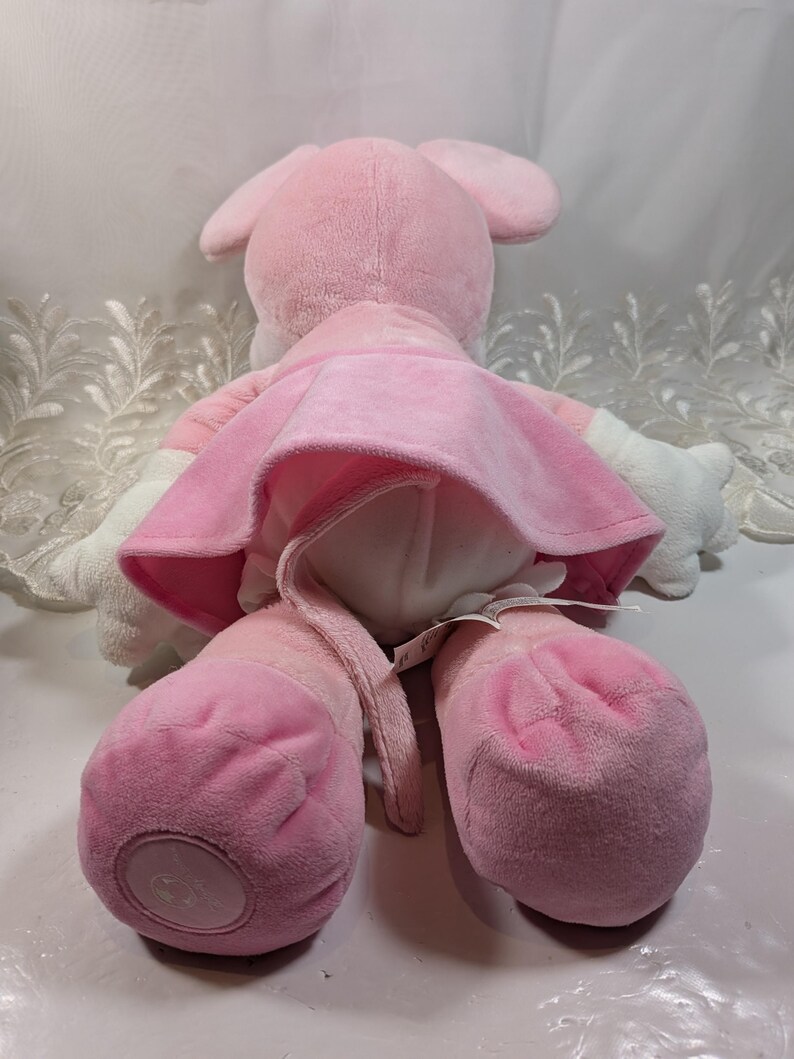 May include: Pink plush mouse wearing a pink dress. The mouse has a long tail and is sitting on a white surface.