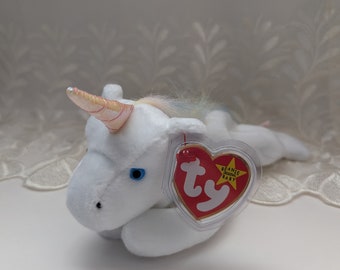 Könnte beinhalten: Ein weißes Plüsch-Einhorn mit einem rosa-goldenen Horn, blauen Augen und einer bunten Mähne. Das Einhorn hat ein rotes herzförmiges Etikett mit der Aufschrift "Beanie Baby".