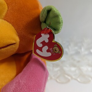 Pode incluir: Brinquedo de macaco de pel&uacute;cia laranja e rosa com uma orelha verde. O macaco tem uma etiqueta Ty que diz "Baby" com um pequeno logotipo de urso.