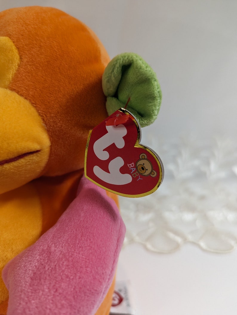 Pode incluir: Brinquedo de macaco de pel&uacute;cia laranja e rosa com uma orelha verde. O macaco tem uma etiqueta Ty que diz "Baby" com um pequeno logotipo de urso.